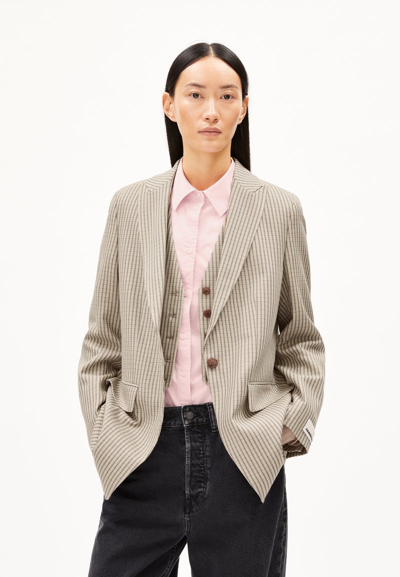 Striped beige blazer with notched lapels, single-breasted front, and two pockets; worn over a light pink shirt and dark jeans.