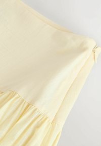Robe jaune clair sans manches avec une taille froncée et une fermeture éclair latérale.