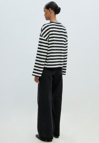 Zwart-witte gestreepte longsleeve top met een relaxte pasvorm, gecombineerd met zwarte hoge taille, losse jeans en zwarte platte schoenen.