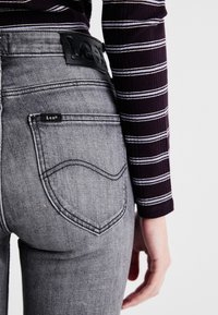 Vaqueros de mezclilla gris con un diseño clásico de cinco bolsillos, costuras reforzadas y una etiqueta de cuero negro en la parte trasera de la cintura.