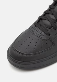 Schwarze Leder-Sneaker mit perforiertem Zehenbereich, flachen schwarzen Schnürsenkeln und einer dicke Gummisohle. Besteht aus glattem Material und hat kontrastierende Nähte.