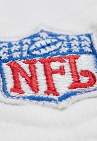 Close-up of embroidered NFL shield logo in red, white, and blue stitching on white fabric background.