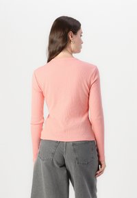 T-shirt a maniche lunghe in cotone ribbed rosa chiaro, con scollatura rotonda e vestibilità slim, abbinato a pantaloni larghi grigi.
