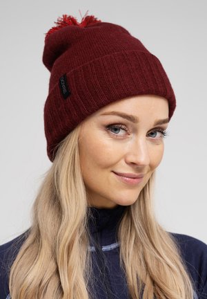 Bordeaux strikket hue med ribbet design, toppet med en rød pom-pom. Har et lille sort mærke med logo. Blød tekstur, varmt materiale.