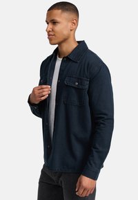 Dunkelblaues Denim-Hemd mit durchgehender Knopfleiste, Kragen und zwei Brusttaschen mit Knöpfen. Weicher Stoff und entspannter Schnitt.