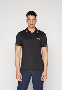 Camiseta polo negra de tela suave, con un tapeta de dos botones, acentos en beige en el cuello y el logo blanco "BOSS" en el pecho.