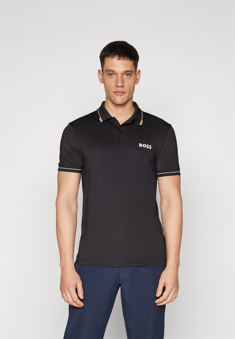 Camiseta polo negra de tela suave, con un tapeta de dos botones, acentos en beige en el cuello y el logo blanco "BOSS" en el pecho.