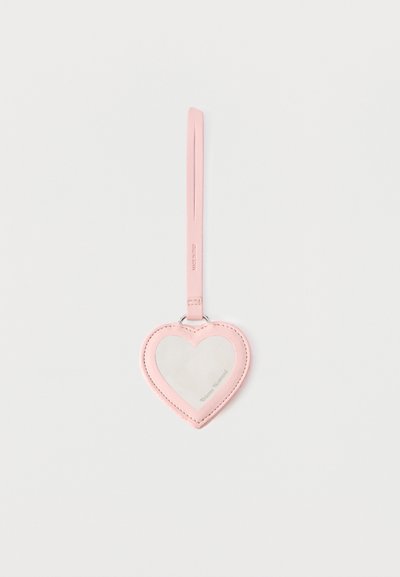 Etiqueta de equipaje de cuero rosa en forma de corazón con ventana transparente y correa adjunta sobre un fondo blanco liso.