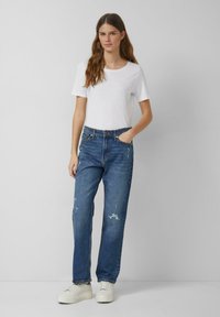 Niebieskie dżinsy o luźnym kroju z detalami przetarć. Połączone z prostą białą bawełnianą koszulką i białymi tenisówkami.