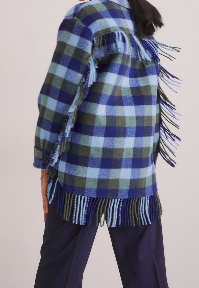 Blå og grøn ternet jakke med frynsekant, lavet af blødt materiale. Har en manchet med knapper og et afslappet fit.