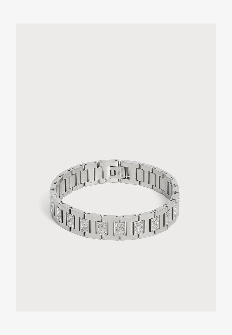 Bracelet en métal argenté avec des segments rectangulaires, certains décorés de petits cristaux transparents, posé à plat sur une surface blanche.