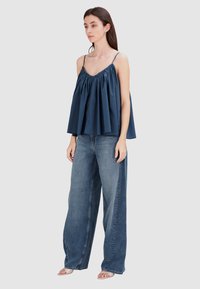 Marineblauw mouwloos topje met een geplooide halslijn en vloeiende stof, gecombineerd met losse, lichtblauwe wijde jeans en platte sandalen.