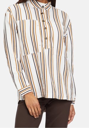 Camisa blanca de manga larga con rayas verticales marrones y mostaza, cuello abotonado, llevada con pantalones marrón oscuro.