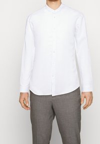 Camicia bianca a maniche lunghe con colletto a band. Realizzata in materiale leggero. Presenta una chiusura con bottoni e un orlo curvo. Texture liscia.