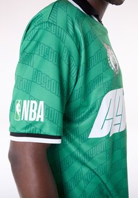 Camiseta de baloncesto verde con "BOSTON" en un patrón repetido, logo de la NBA en la manga y un detalle blanco en el frente.