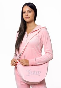 Roze fluwelen sweatshirt en bijpassende broek, met een crossbodytas met strassletters die "Juicy" spellen. Gladde textuur, minimalistisch ontwerp.