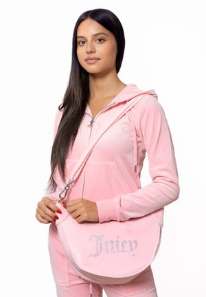 Rosa Samt-Sweatshirt und passende Hose, mit einer Umhängetasche, die mit Strassbuchstaben "Juicy" beschriftet ist. Glatte Textur, minimalistisches Design.