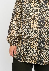 Lässige Bluse mit einem schwarz-beigen Blumenmuster, langen Puffärmeln mit elastischen Bündchen und leichtem V-Ausschnitt.