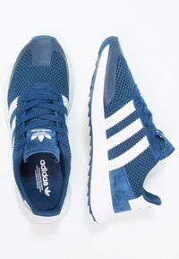 Námořnické modré sportovní boty s prodyšným svrškem, semišovými akcenty a bílým designem se třemi pruhy. Mají strukturovanou podrážku a polstrovaný límec.