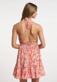 Rot-weiße gemusterte Halbdress mit einem ausladenden Rock, offenem Rücken und verstellbaren Bindebändern am Hals und in der Taille. Mit einem Rüschensaum.