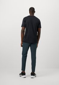 Sort kortærmet T-shirt parret med teal tapered bukser. Modellen ses fra ryggen, hvilket fremhæver det enkle design og den atletiske pasform.