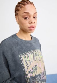 Lichtgrijze sweatshirt met geribbelde textuur en een ronde hals, voorzien van een kleurrijke grafische print met tropische afbeeldingen.