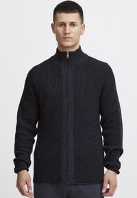 Mörk marinblå zip-up tröja i texturerad stickad tyg, med hög krage och figurnära ärmar, samt en slät dragkedja framtill.