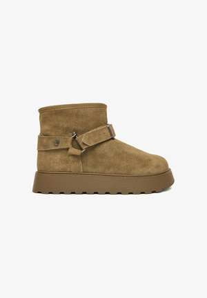 Brauner Wildleder-Stiefelette mit dicker Gummisohle und verstellbarem Riemen mit Metallschnalle an der Seite.
