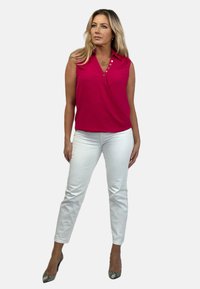 Fuksjowa bezrękawnikowa bluzka z kołnierzykiem i guzikami, zestawiona z białymi spodniami slim-fit i wzorzystymi szpilkami.