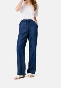 Breda denimbyxor i mörkblått, med resårdragsko i midjan och sidofickor. Kombinerat med en ljusfärgad V-ringad topp.