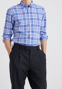 Blå och vit rutig skjorta med knäppning nedtill, kombinerad med mörkgrå byxor med veck och sidofickor.