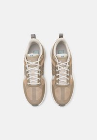 Un paio di sneakers sportive beige e bianche con lacci bianchi e linguette, viste dall'alto su uno sfondo chiaro.