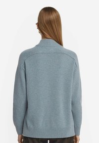 Ljusblå stickad tröja med hög krage, nedhasade axlar och ribbad nederkant. Mjuk textur med minimala sömmar och en avslappnad passform.