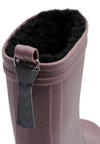 Stivale da pioggia in gomma marrone con esterno testurizzato e interno in fleece nero. Presenta una linguetta grigia attaccata con un anello di metallo.