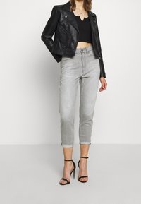 Jeans de mezclilla gris con detalles desgastados, con puños cortados y enrollados, combinados con una chaqueta de cuero negra recortada y tacones de aguja negros.