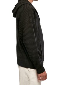 Huvtröja i mörkgrå stickad tyg, med ribbad struktur, långa ärmar och avslappnad passform med sidofickor.