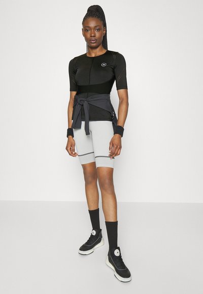 Black short-sleeve athletic top with mesh details, grey high-waisted shorts, and black high-top sneakers with white soles. Black wristbands and belt.
