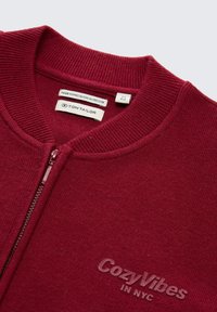 Burgunderfarbene Jacke mit Reißverschluss aus ökologischer Viskose. Mit geripptem Kragen und geprägtem Detail "CozyVibes IN NYC". Weiche Textur.