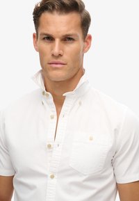 Witte kortemouwen shirt met een kraag met knopen, voorzien van een borstzakje en kleine, lichte knopen. Gladde katoenstof.