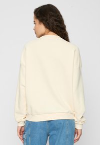 Cremfarbener, übergroßer Sweater mit rundem Ausschnitt, überschnittenen Schultern und gerippten Bündchen, kombiniert mit hellblauen Jeans.