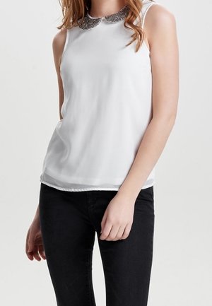 Top bianco senza maniche con colletto decorativo e dettagli di perline. Il tessuto è liscio e leggermente traslucido, abbinato a pantaloni neri.