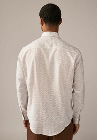 Cămașă cu mânecă lungă de culoare crem deschis, cu un model geometric în nuanțe de portocaliu și albastru. Guler cu nasturi, tiv curbat și material texturat.