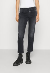 Jeans in denim scuro con una vestibilità slim, caratterizzati da una vita a media altezza e un leggero sbiadimento. Abbinati a stivali da combattimento neri con lacci.