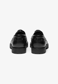 Chaussures en cuir noir avec une finition lisse, un design arrondi et des semelles en caoutchouc épaisses. Comprend des coutures doubles et des accents métalliques.