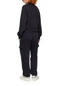 Czarna skrócona bluza z mankietami, zestawiona z pasującymi spodniami cargo z kieszeniami bocznymi i luźnym krojem. Białe trampki dopełniają stylizację.