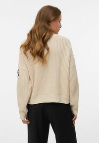 Maglione lavorato a maglia color crema con vestibilità ampia, polsini a coste e orlo corto. Presenta un motivo testurizzato e un dettaglio ricamato sulla manica.