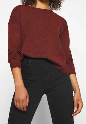 Maglione a maglia bordeaux con vestibilità rilassata, ampiascollo a barca, e polsini a costine, abbinato a jeans neri a vita alta.
