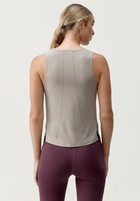 Top beige aderente con scollatura tonda. Presenta perforazioni verticali sul retro per la ventilazione. Abbinato a leggings a vita alta color bordeaux.