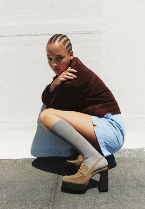 Tan platform shoes with stacked heels, paired with gray knee-high socks. The outfit includes a brown suede jacket and a blue striped skirt.