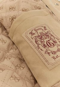 Bežna prešita jakna z zamšastimi detajli. Ima burgundski logotip na ovratniku in subtilen monogram vzorec na notranji podlogi.